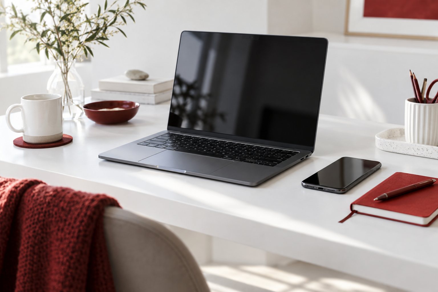 Laptop and phone on a bright desk with a red notebook